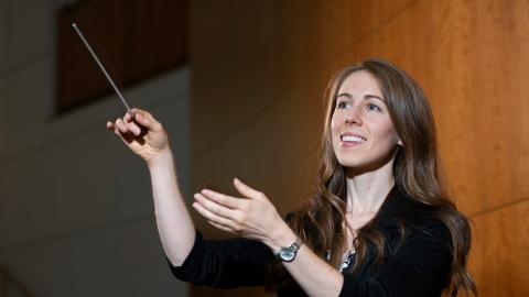 a UMD student conducting with a baton in their right hand and slightly smiling.